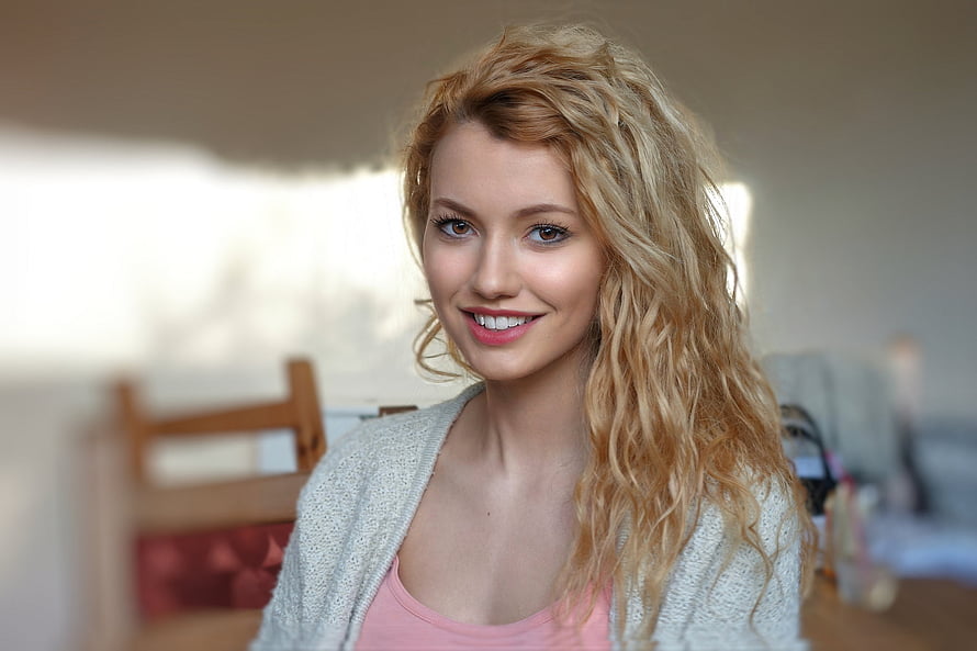 Smiling Woman With Curly Blonde Hair Wearing A Light Cardigan In A Bright Indoor Setting HD wallpaper
