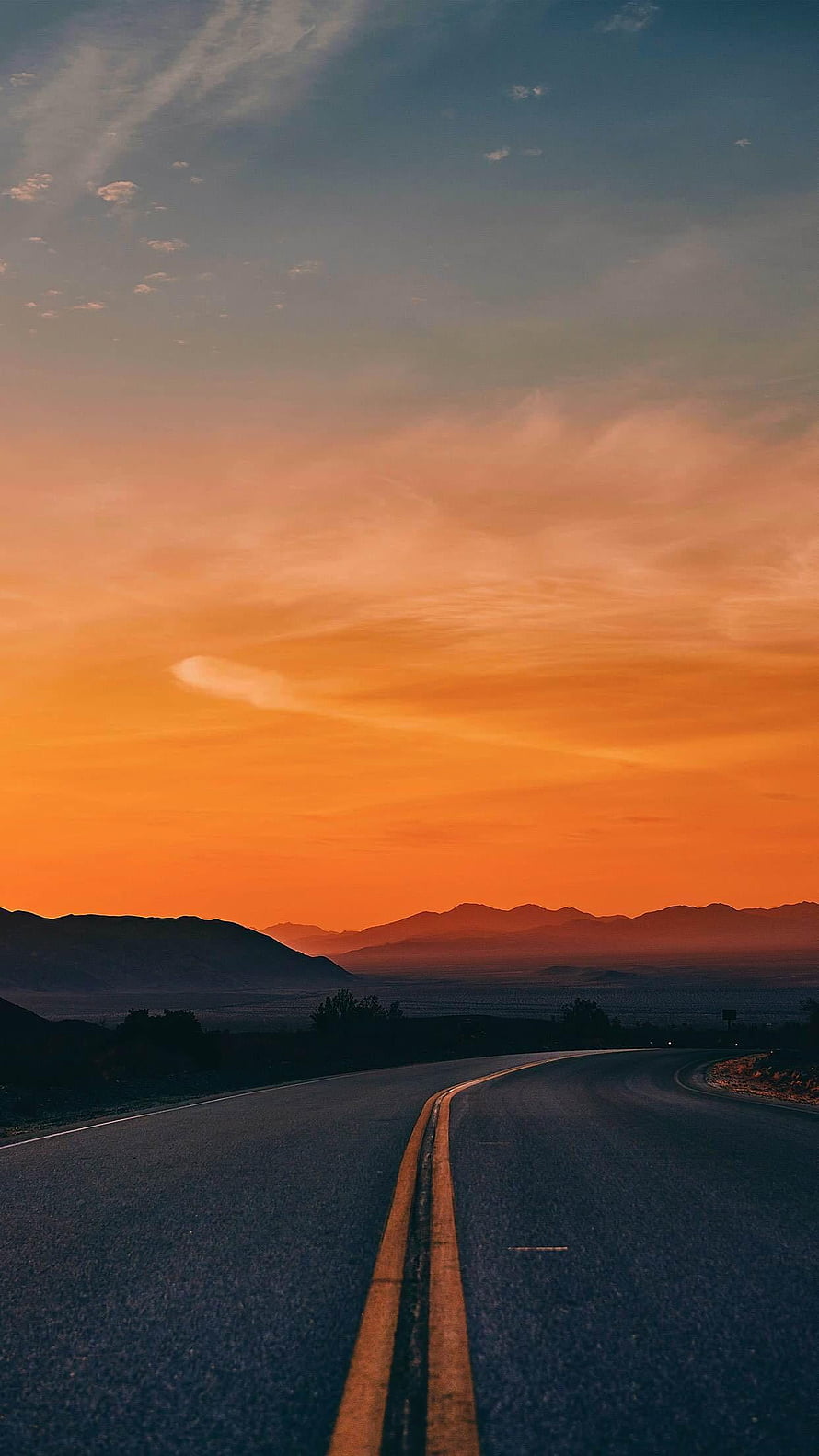 Empty Highway Stretching Toward Distant Mountains Under a Vibrant Orange Sunset Sky HD phone wallpaper