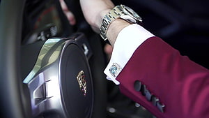 Close-up of a luxury wristwatch and cufflink on a maroon suit sleeve inside a car HD wallpaper