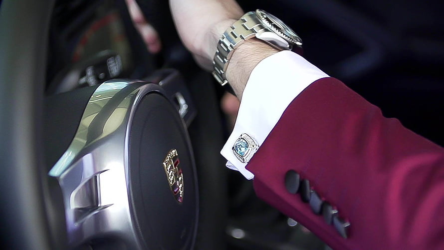 Close-up of a luxury wristwatch and cufflink on a maroon suit sleeve inside a car HD wallpaper