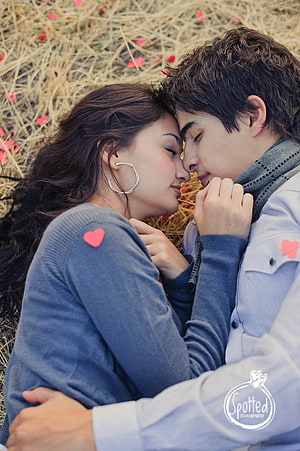 Romantic couple embracing with foreheads touching in a field of dry grass and scattered petals HD phone wallpaper