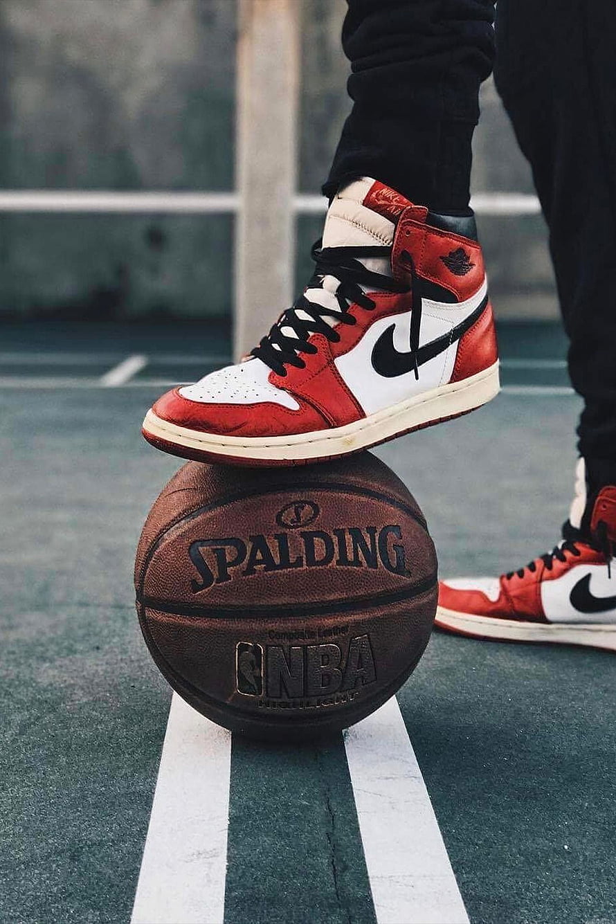 Air Jordan 1 High Chicago sneakers balanced on a Spalding basketball on an outdoor court HD phone wallpaper