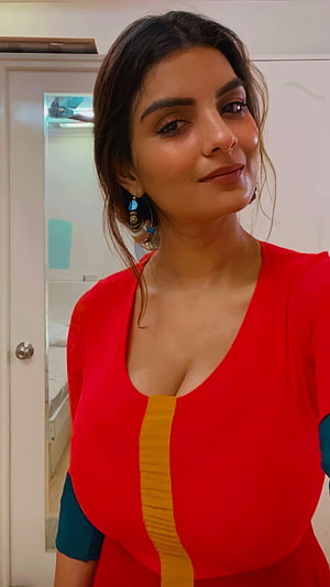 Anveshi Jain in a vibrant red and yellow dress with teal accents and statement earrings HD phone wallpaper
