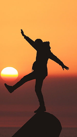 Silhouette of a man balancing on a rock at sunset with arms outstretched HD phone wallpaper
