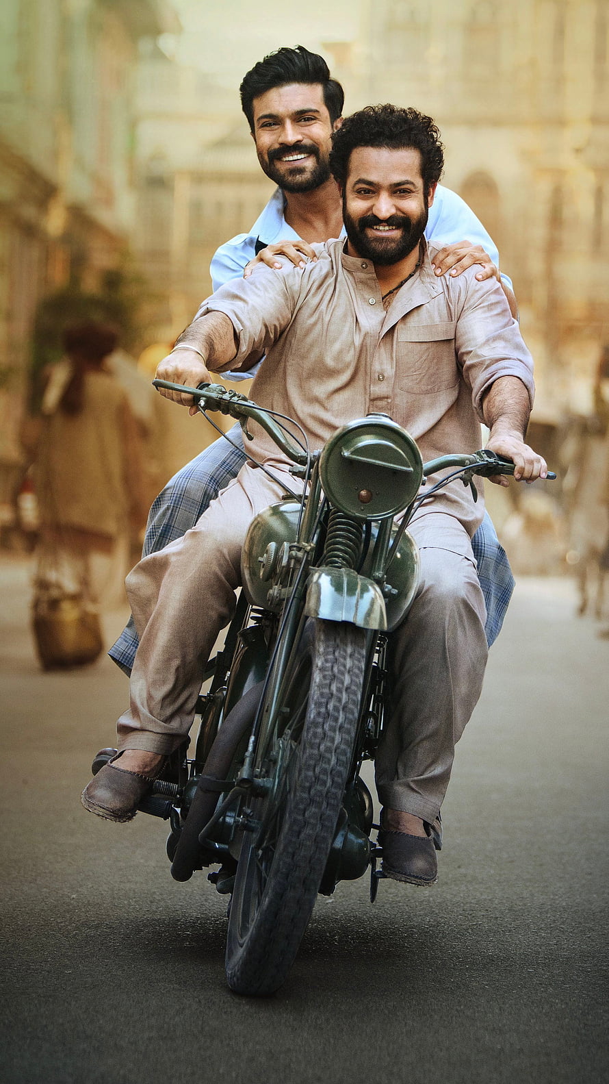 RRR Movie Still: Ram Charan and NTR Riding a Vintage Motorcycle Through a Historic Street HD phone wallpaper