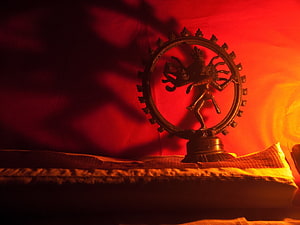Nataraja bronze statue in dramatic red and orange lighting on a cushioned surface HD wallpaper