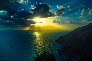 Golden Sunburst Breaking Through Dramatic Clouds Over a Vast Ocean and Coastal Cliffs HD wallpaper