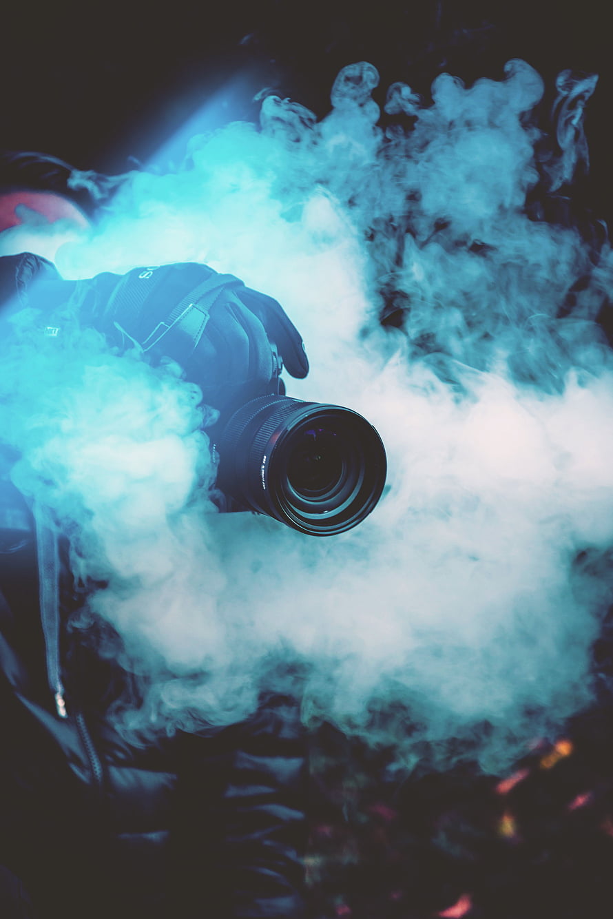 Professional DSLR Camera Emerging From Swirling Blue Smoke Against Dark Background HD phone wallpaper