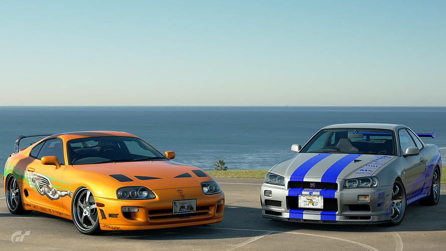 Toyota Supra and Nissan Skyline GT-R parked side by side on a coastal road overlooking the ocean HD wallpaper