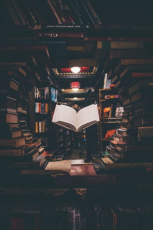 Open Book Floating in a Dimly Lit Library Aisle Surrounded by Stacked Volumes HD phone wallpaper