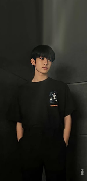 ENHYPEN Heeseung in a black graphic t-shirt against a dark textured wall HD phone wallpaper