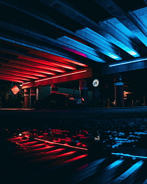 Neon-lit sports car parked under a concrete overpass with red and blue reflections in water HD phone wallpaper