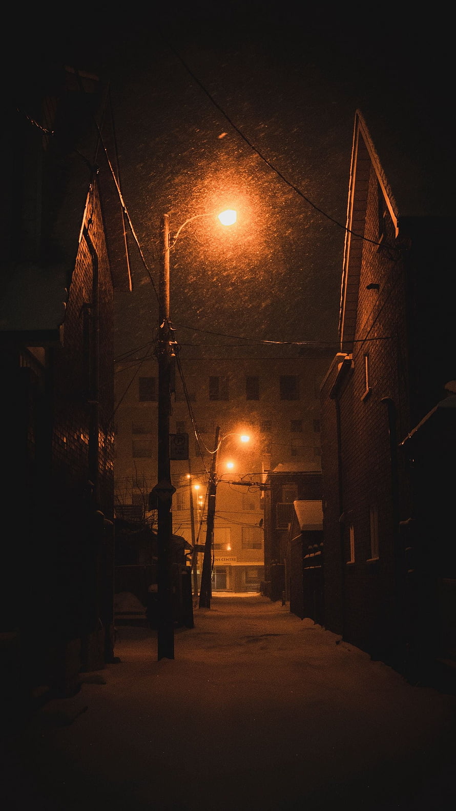 Snowy Urban Alleyway at Night Illuminated by Warm Street Lamps HD phone wallpaper