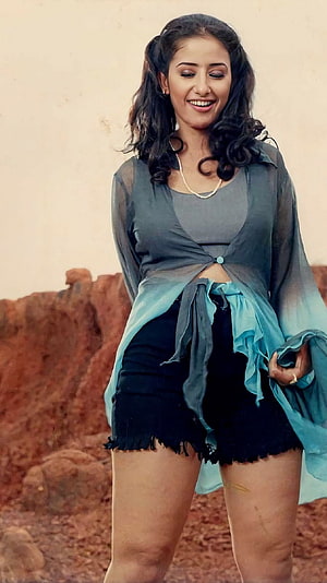 Manisha Koirala in a Flowing Blue Drape and Black Shorts Against a Rusty Rock Wall HD phone wallpaper