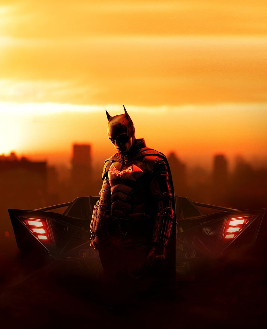Batman standing before the Batmobile against a fiery orange sunset with a city skyline in the background HD phone wallpaper