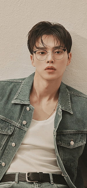 Song Kang in a denim jacket and round glasses against a textured beige wall HD phone wallpaper