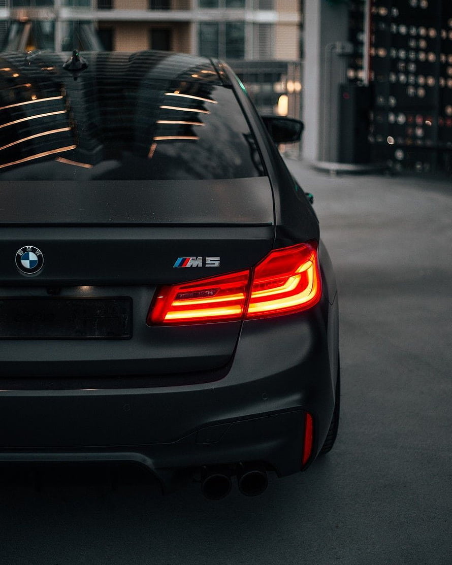 Rear View of a Matte Black BMW M5 F90 with Glowing LED Taillights and Dual Exhausts HD phone wallpaper