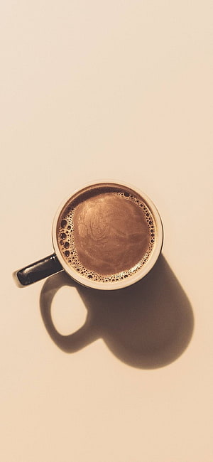 Top-down view of a frothy espresso in a white ceramic mug with a long shadow on a cream background HD phone wallpaper