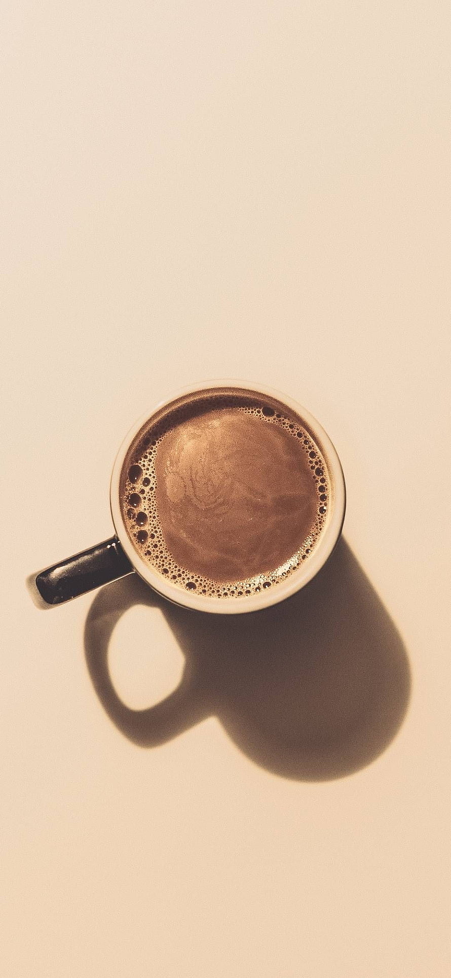 Top-down view of a frothy espresso in a white ceramic mug with a long shadow on a cream background HD phone wallpaper