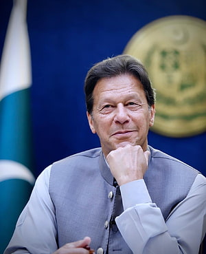 Imran Khan in formal grey attire with Pakistan flag and national emblem in background HD phone wallpaper