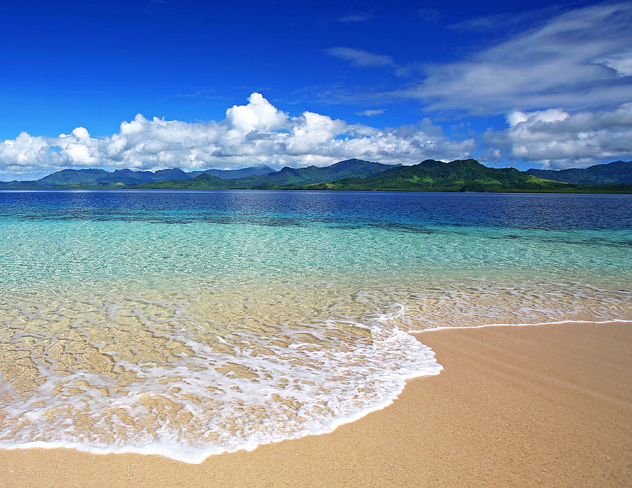 Tropical Beach with Turquoise Water, White Sand, and Distant Green Mountains Under a Blue Sky HD wallpaper