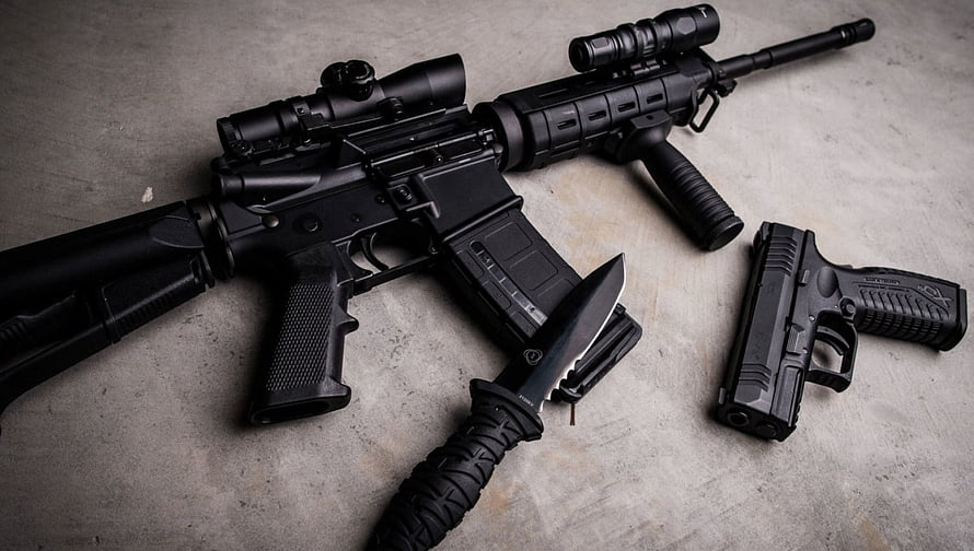 Black AR-15 rifle with tactical scope, vertical foregrip, combat knife, and pistol arranged on concrete surface HD wallpaper
