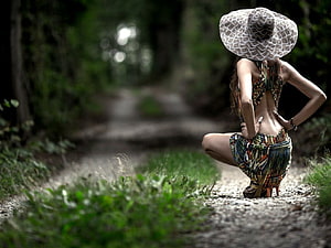Woman in patterned outfit and wide-brimmed hat crouching on a forest path HD wallpaper