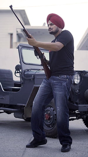 Sidhu Moose Wala in red turban holding rifle beside vintage military jeep HD phone wallpaper