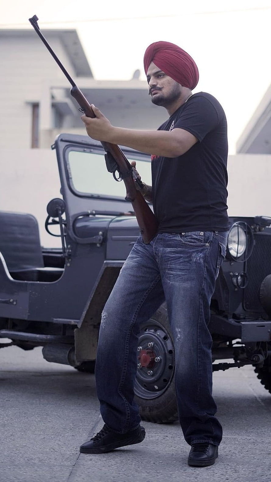 Sidhu Moose Wala in red turban holding rifle beside vintage military jeep HD phone wallpaper