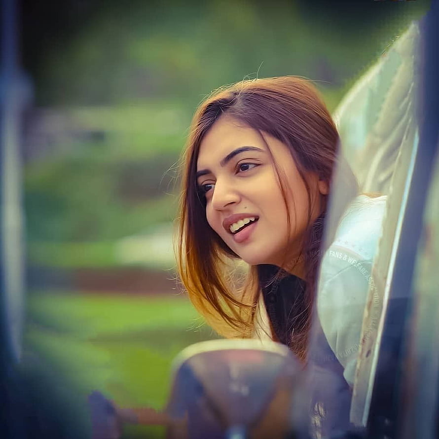 Nazriya Nazim smiling warmly while looking out from a vehicle window with a soft green background HD phone wallpaper
