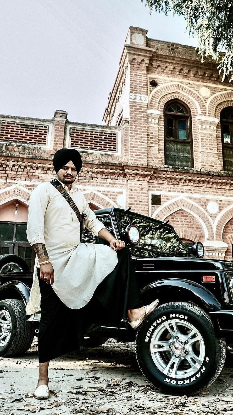 Sidhu Moose Wala in Traditional Attire Leaning Against a Black Jeep in Front of a Historic Brick Building HD phone wallpaper