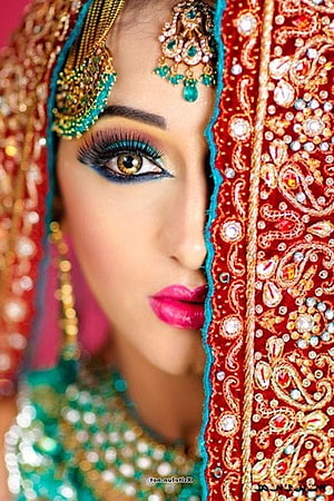 Close-up portrait of an Indian bride wearing ornate red and gold embroidered dupatta with traditional jewelry HD phone wallpaper