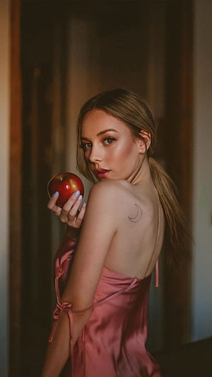 Ester Exposito in a pink satin dress holding a red apple with a crescent moon tattoo HD phone wallpaper