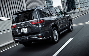 2021 Toyota Land Cruiser 300 Series ZX Black SUV Rear Three-Quarter View on Urban Highway HD wallpaper
