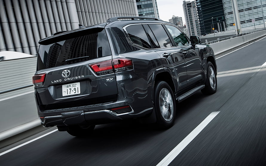 2021 Toyota Land Cruiser 300 Series ZX Black SUV Rear Three-Quarter View on Urban Highway HD wallpaper