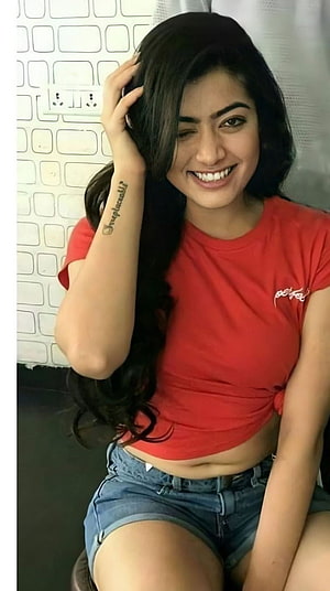 Rashmika Mandanna smiling in a red crop top and denim shorts HD phone wallpaper