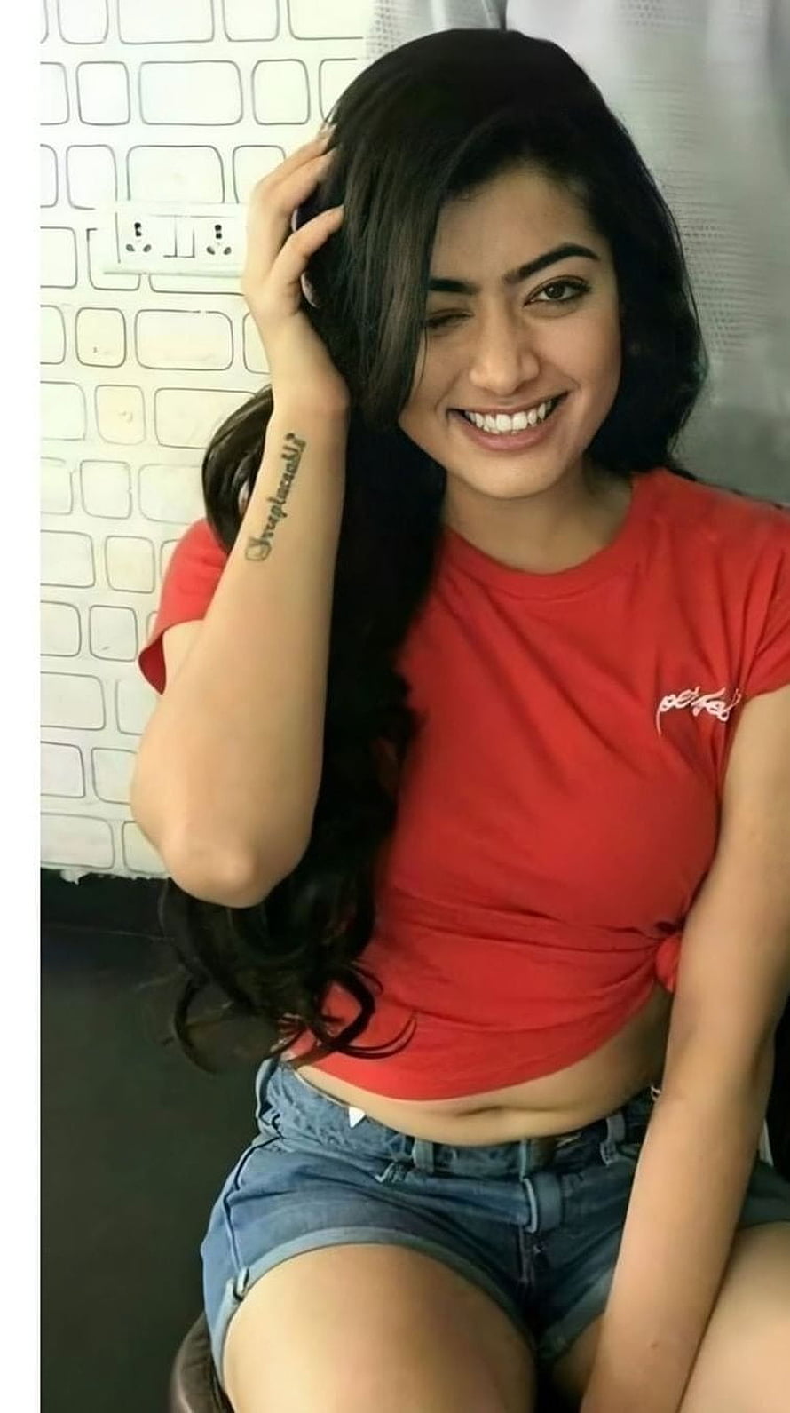 Rashmika Mandanna smiling in a red crop top and denim shorts HD phone wallpaper