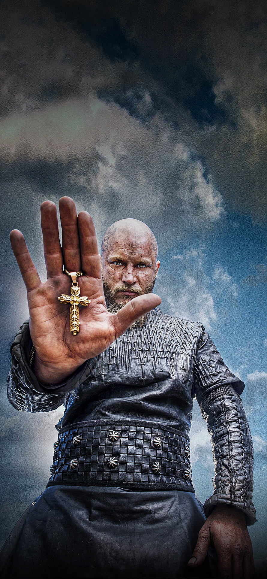 Ragnar Lothbrok holding a golden cross in a dramatic Viking costume against a stormy sky HD phone wallpaper