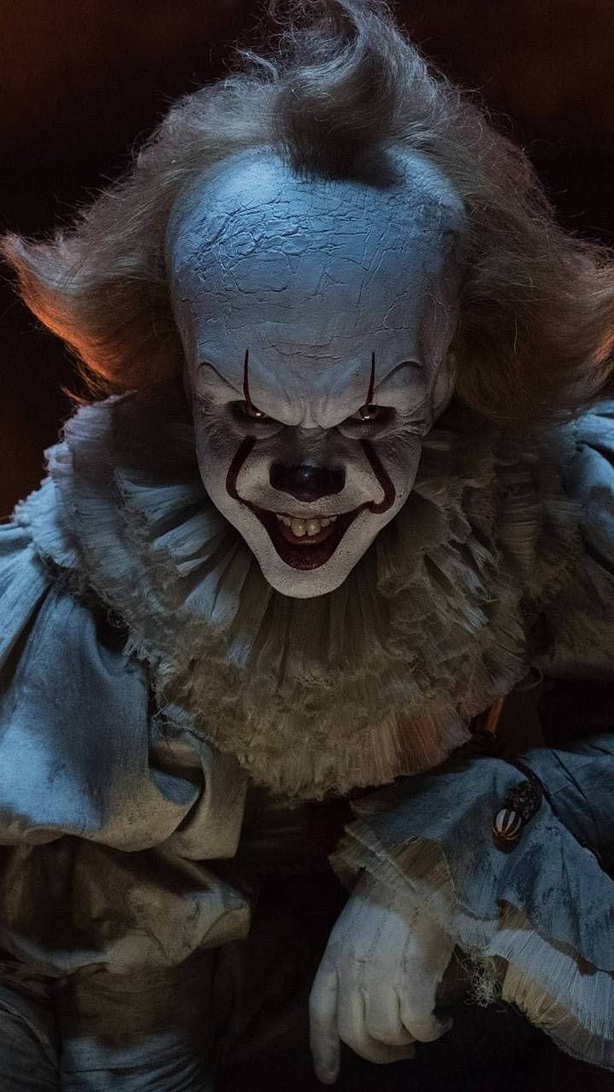 Terrifying Pennywise the Dancing Clown with cracked white face paint and menacing grin in dark horror setting HD phone wallpaper