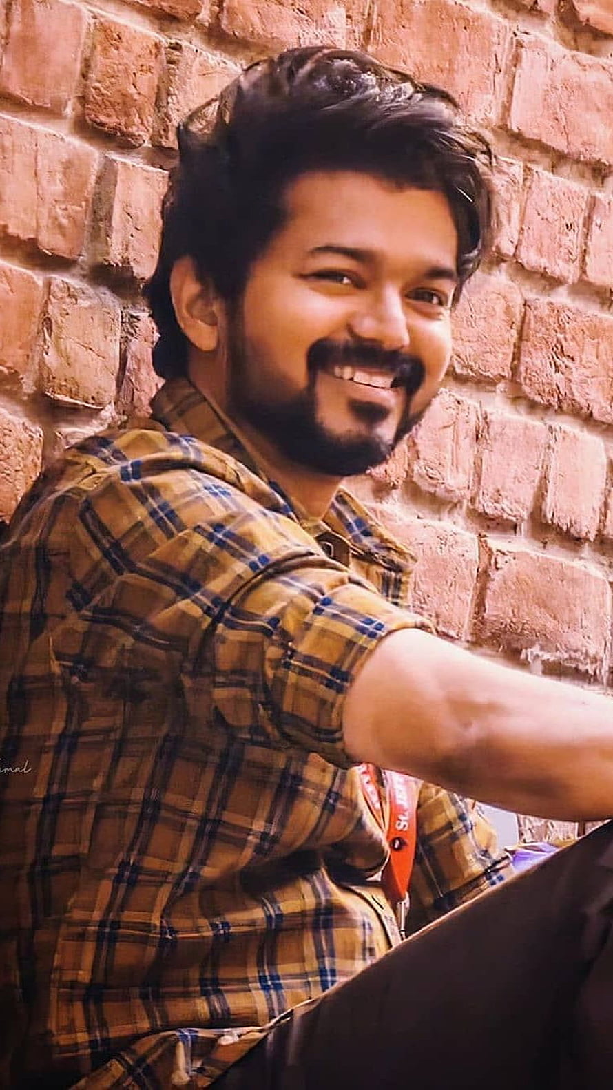 Vijay Thalapathy Smiling Portrait in Plaid Shirt Against Brick Wall HD phone wallpaper