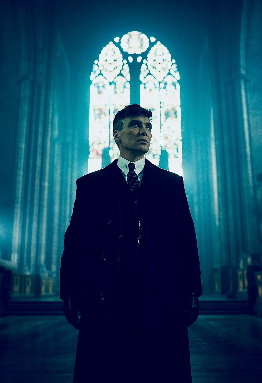 Thomas Shelby in a dark overcoat standing before a glowing stained glass window in a cathedral HD phone wallpaper
