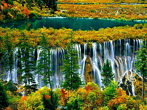 Vibrant autumn foliage surrounding a cascading waterfall and turquoise alpine lake HD wallpaper