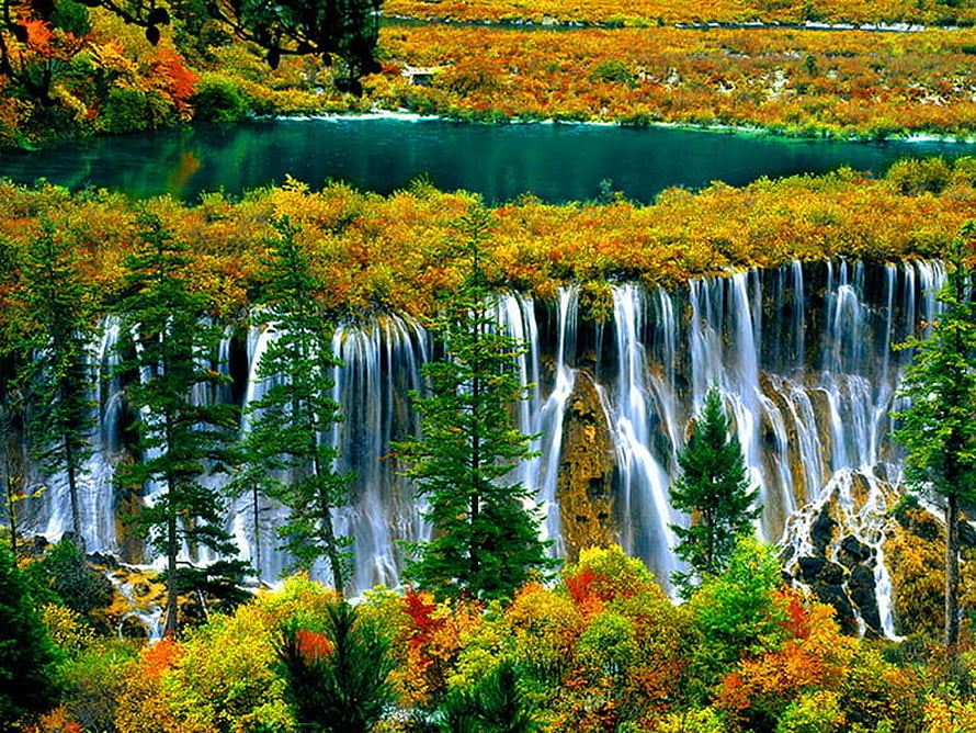 Vibrant autumn foliage surrounding a cascading waterfall and turquoise alpine lake HD wallpaper