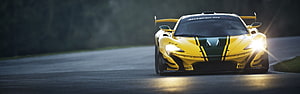 Yellow McLaren 720S GT3 race car with green racing stripes on a track at dusk HD wallpaper