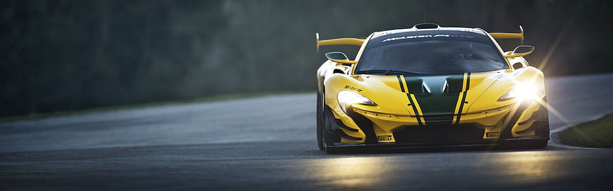 Yellow McLaren 720S GT3 race car with green racing stripes on a track at dusk HD wallpaper
