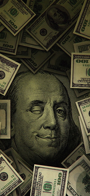 Close-up of Benjamin Franklin portrait on scattered US one hundred dollar bills with dark moody aesthetic HD phone wallpaper