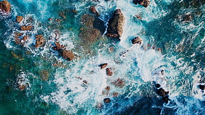 Aerial View of Turquoise Ocean Waves Crashing Against Rocky Coastline HD wallpaper