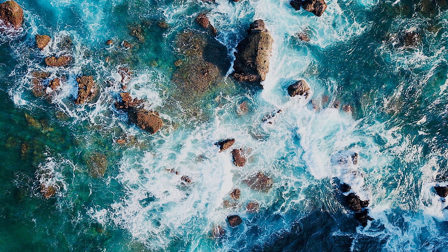 Aerial View of Turquoise Ocean Waves Crashing Against Rocky Coastline HD wallpaper