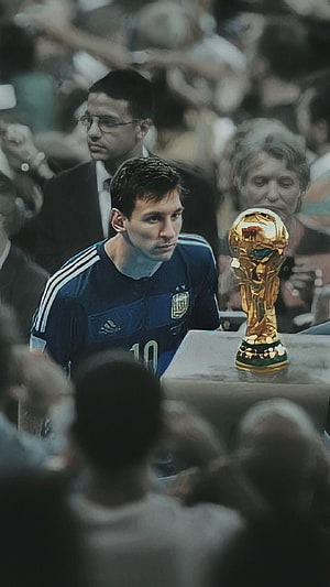 Lionel Messi in Argentina jersey gazing at the FIFA World Cup trophy in a somber stadium scene HD phone wallpaper