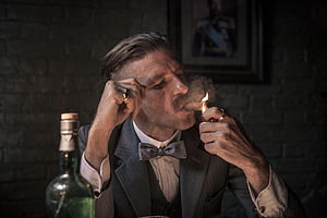 Arthur Shelby Lighting a Cigar in a Dimly Lit Room Wearing a Suit and Bow Tie HD wallpaper